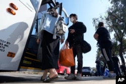 FILE - A couple from China board a bus to the airport after crossing the border and being dropped off by Border Patrol agents at a transit center in San Diego, California, Oct. 18, 2023.