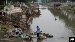 Residents wash their suitcase and belongings on a damaged bank of a canal clogged with flood debris in the aftermath of river flooding in the Mentougou district on the outskirts of Beijing, Aug. 7, 2023.