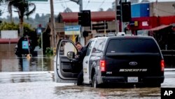Seorang wakil sheriff mengecek kendaraannya saat melintasi jalan yang tergenang banjir di kawasan Pajaro, Monterey County, California, Senin, 13 Maret 2023. (Foto: Noah Berger/AP Photo)