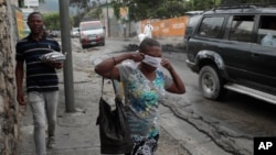 FILE - A woman walks past authorities removing the bodies of men that were set on fire by a mob in Port-au-Prince, Haiti, April 25, 2023, a day after a mob pulled the suspected gang members from police custody and beat and burned them to death.
