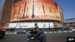 A man rides a motorbike past a billboard depicting Iranian ballistic missiles in service in Tehran on April 19, 2024. 