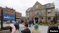 FILE - Customers wait outside Silicon Valley Bank (SVB) branch in Wellesley, Massachusetts, March 13, 2023. Moody’s Investors Service said depositor runs for cash in their accounts at SVB and two other banks have sparked fears of broader problems in the U.S. banking system.