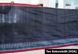 សំពត់សូត្រពណ៌​ខ្មៅ​ដែល​មាន​គោមជារូបថូផ្កានេះ ត្រូវបាន​ត្បាញ​ដោយ​ស្ត្រីចាម​ក្រោម​គម្រោង​សូត្រចាម Color of Memory ឬ​ពណ៌​នៃ​ការ​ចងចាំ ដែល​ត្រូវបាន​ផ្តួចផ្តើម​ឡើង​ដោយ​វិទ្យាស្ថានស្លឹករឹត នៅភ្នំពេញ កាលពីថ្ងៃទី ២៧ ខែកុម្ភៈ ឆ្នាំ ២០២៣។ (ទែន សុខស្រីនិត/វីអូអេ)