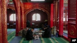 FILE - Muslim men read the Quran while waiting for the time to break their fast during the first day of Ramadan at the Niujie Mosque in Beijing, March 12, 2024. 