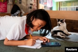 FILE - A student answers her learning module following the suspension of in-person classes, at her family's empty store, in Manila, Philippines, April 26, 2024. (REUTERS/Lisa Marie David)