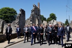 French President Emmanuel Macron (2ndL), the Mayor of Oradour-sur-Glane (L), and German President Frank-Walter Steinmeier (2ndR) walk along a street in Oradour-sur-Glane, June 10, 2024.