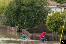 Un hombre y un niño "navegan" en bicicletas por las calles inundadas de Watsonville, California, el 11 de marzo de 2023.