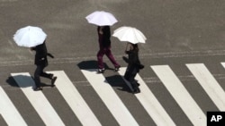 People holding parasols cross a street in scorching heat at Ginza district in Tokyo, Japan, Aug. 4, 2023.