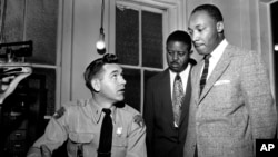 FILE - The Rev. Martin Luther King Jr., right, accompanied by Rev. Ralph D. Abernathy, center, is booked by city police Lt. D.H. Lackey in Montgomery, Alabama, on Feb. 23, 1956.