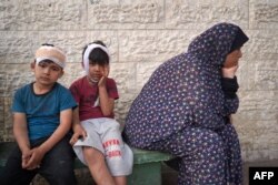 Injured Palestinian boys wait with their families to identify the bodies of relatives killed in an Israeli bombardment, in the yard of the Al-Aqsa Martyrs Hospital in Deir al-Balah in the Gaza Strip, May 11, 2024.