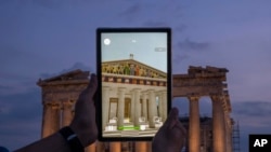 FILE - A man holds up a tablet showing a digitally overlaid virtual reconstruction of the ancient Parthenon temple, at the Acropolis Hill in Athens, Greece, June 13, 2023. 