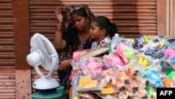 People sit in front of a table fan to cool off on a hot summer afternoon in Varanasi, India, May 29, 2024.