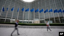 FILE - European Union flags wave in the wind as pedestrians walk by EU headquarters in Brussels, on Sept. 20, 2023.