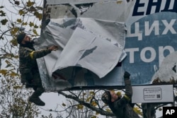 FILE - Ukrainian soldiers remove Russian posters in Kherson, Ukraine, Sunday, Nov. 13, 2022. (AP Photo/LIBKOS)