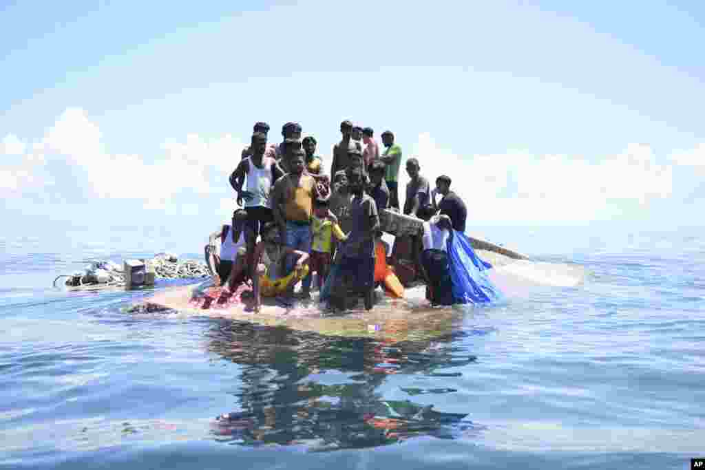 Rohingya refugees stand on their capsized boat before being rescued in the waters off West Aceh, Indonesia.