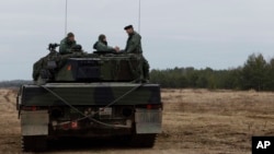 Ukrainian and Polish soldiers sit on top of a Leopard 2 tank during training at a military base and test range in Swietoszow, Poland, Feb. 13, 2023.