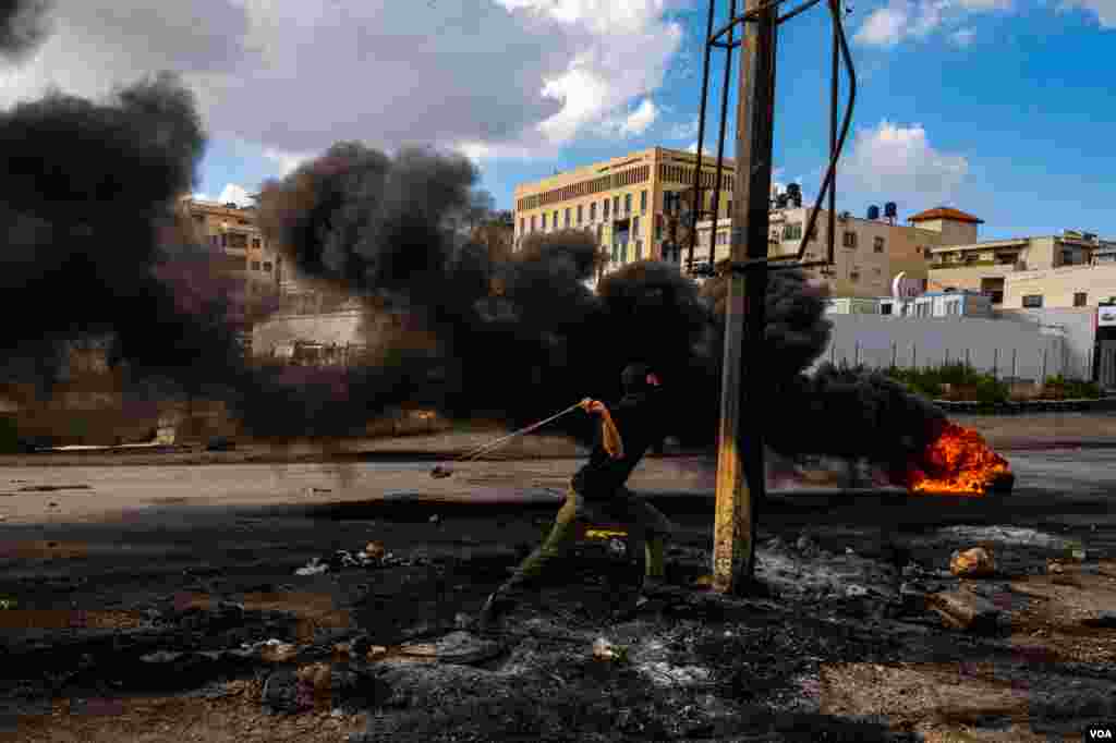 A Palestinian protester throws rocks at Israeli soldiers with a slingshot, on the outskirts of Ramallah, Oct. 20, 2023. (Yan Boechat/VOA)