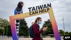 FILE - A woman walks by an arch reading "Taiwan can help" next to the building of the United Nations Offices in Geneva on the opening day of the WHO's World Health Assembly in Geneva, on May 24, 2021. 