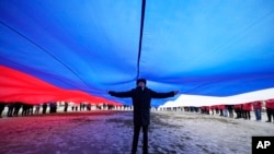 FILE - A Navy school cadet stands under a giant Russian flag during an action to mark the ninth anniversary of the Crimea annexation from Ukraine, in St. Petersburg, Russia, March 18, 2023. 
