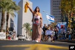 A woman, with a photograph of a child who was abducted during the unprecedented Hamas attack on Israel, hands out yellow ribbons in central Tel Aviv, Israel, Oct. 25, 2023. The ribbons are the symbol for those actively asking for the release of Israeli hostages.