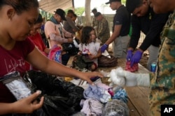Venezuelan migrant Rashell Soler sits on a table as her mother, Vilkeine Montero, goes through an inspection of her bag at a temporary camp in Lajas Blancas, Panama, June 28, 2024, after walking across the Darien Gap from Colombia.