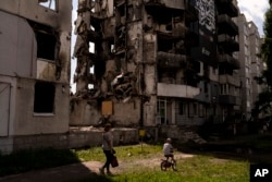 A woman and a boy make their way past an apartment building destroyed in Russian attacks in Borodyanka, Ukraine, Aug. 2, 2023.