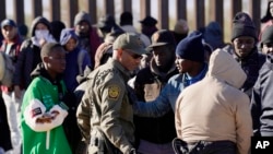 FILE - A member of US Customs and Border Protection tries to control a group of migrants as hundreds gather along the border after breaking through gaps in the border wall Dec. 5, 2023, in Lukeville, Ariz. 