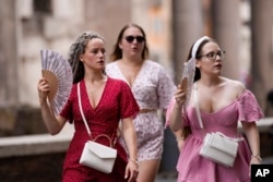 FILE - Tourists use foldable fans to cool off as they visit Rome, July 22, 2023.