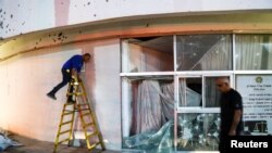 A man walks as another works outside a damaged building after rockets from Lebanon were fired into Israel, in Shlomi, northern Israel, April 6, 2023.