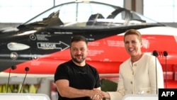 Ukrainian President Volodymyr Zelenskyy, left, and Danish Prime Minister Mette Frederiksen shake hands at a press conference in front of a F-16 fighter jet in the hangar of the Skrydstrup Airbase in Vojens, northern Denmark, on Aug. 20, 2023.