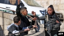 A member of the Israeli security forces speaks with Palestinian boys during the Friday noon prayer in the east Jerusalem neighborhood of Ras al-Amud, on Jan. 19, 2024 as age restrictions have been imposed to access the Al-Aqsa Mosque compound.