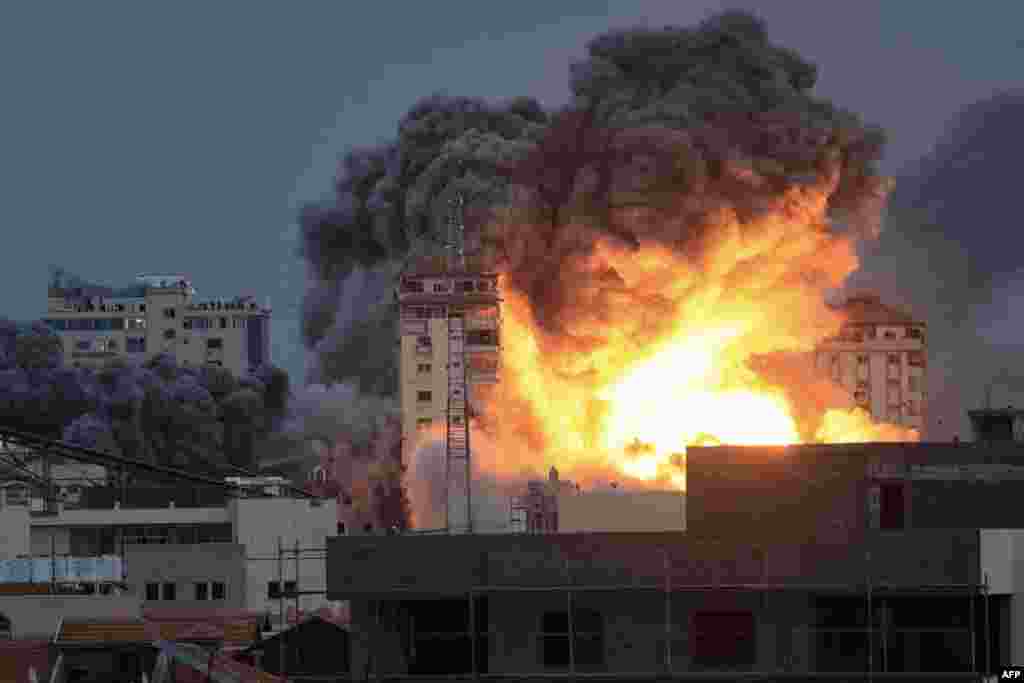 People standing on a rooftop watch as a ball of fire and smoke rises above a building in Gaza City, Oct. 7, 2023 during an Israeli airstrike that hit the Palestine Tower building.&nbsp;
