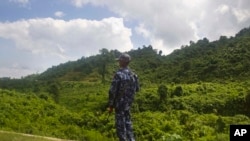 FILE - A Myanmar police officer stands on a road as they provide security at a checkpoint in Buthidaung, Rakhine State, western Myanmar on May 28, 2017. 