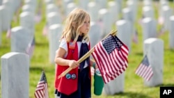 American Heritage Girl Isabel Lennon carries flags to be placed on head stones at the Middle Tennessee Veterans Cemetery in honor of Memorial Day, May 25, 2024, in Nashville, Tenn. 