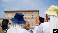 A nun films Pope Francis as he recites the Angelus noon prayer from the window of his studio overlooking St. Peter's Square, at the Vatican, Aug. 27, 2023