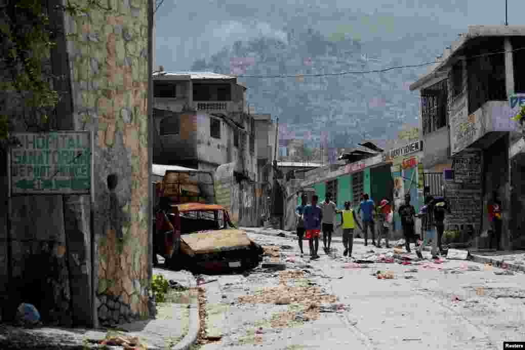 Луѓето поминуваат покрај оштетен автомобил во населбата Карфур Феј, која беше напуштена поради насилство од бандите, во Порт-о-Пренс, Хаити, 19 март 2024 година.