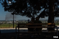 A couple sitting on the main Kupiansk square watches the smoke rising in the forests after a volley of Russian shells hit the outskirts of the city on Aug. 19, 2023. (Yan Boechat/VOA)