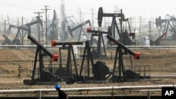 FILE - A worker walks near pumpjacks operating at the Kern River Oil Field in Bakersfield, Calif., Jan. 16, 2015.