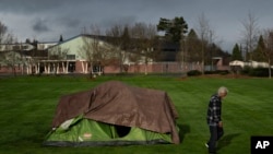 With Fruitdale Elementary School in the background, a homeless person walks near a tent in Fruitdale Park, March 23, 2024, in Grants Pass, Ore. The rural city in southern Oregon has become the unlikely face of the nation's homelessness crisis.