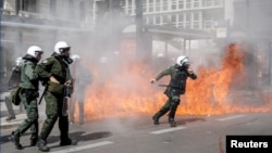 A riot police officer prepares to throw a stun grenade next to flames as clashes take place during a demonstration following the collision of two trains, near the city of Larissa, in Athens, March 5, 2023. 