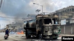 FILE - A person on a scooter rides past a damaged water tanker that was set afire during a protest by tribal groups in Churachandpur, in the northeastern Indian state of Manipur, May 4, 2023.
