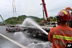 A firefighter sprays water on the remains of a car in the aftermath of the collapse of a highway section on the Meizhou-Dabu Expressway in Meizhou, south China's Guangdong province, May 1, 2024, in this photo released by Xinhua News Agency.
