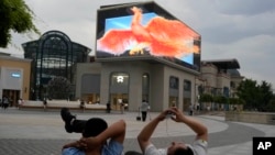 FILE - Men rest near a screen depicting a phoenix at a mall in Beijing, June 11, 2024. China kept a key lending rate unchanged June 17 as data showed signs of persistent weakness in manufacturing and the real estate sector.