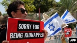 A woman holds a sign as other raise Israeli flags during a rally near the house of Israeli war cabinet member Benny Gantz in Rosh Haayin, Israel, on May 3, 2024, calling on the government to reach an agreement for the release of all hostages.