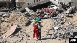 A Palestinian child walks with a stuffed bear recovered from the rubble of a destroyed building following Israeli bombardment in Khan Yunis on June 21, 2024.