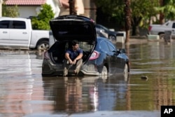 Dorian Padilla sits in his car as he waits for a tow after he got stuck in the mud on a street Cathedral City, California, Aug. 21, 2023.