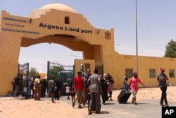 Evacuees carry their luggage as they cross into Egypt through the Argeen land port after being evacuated from Sudan to escape the conflict, on the international border lines between Egypt and Sudan, April 27, 2023.
