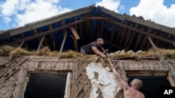 People cover a roof with tarps after their house was hit by a Russian airstrike near the Russian-Ukrainian border in Sumy region, Ukraine, Aug. 15, 2024.