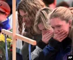 FILE - Columbine High School students from left, Darcy Craig, Molly Byrne and Emily Dubin stop to pay their respects at a make shift memorial set up in a park near the high school, April 22, 1999.