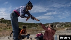 An aid worker provides food to a six-year-old migrant from Guatemala and her seven-year-old brother after they crossed into the United States from Mexico with their family in Jacumba Hot Springs, California, May 20, 2024.
